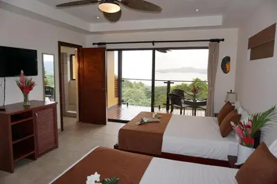 a bedroom with two beds and a balcony with a television at Eco Boutique Hotel Vista Las Islas Reserva Natural in Paquera