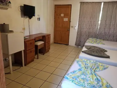a room with two beds and a desk and a television at Mapi's Cabins in Paquera