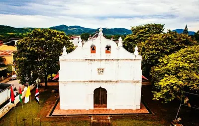 a white building with trees and mountains in the background at Hoja Azul in Hojancha