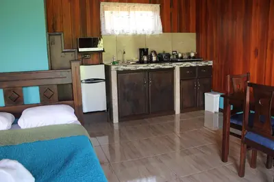 a kitchen with wooden cabinets and a table and a bed at Cabañas Sueños del Arenal in Fortuna