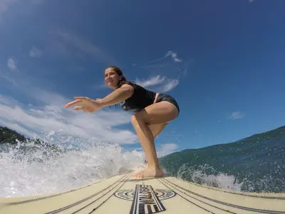 a woman riding a wave on a surfboard on a beach at Hotel Perico Azul & Surf Camp in Jacó