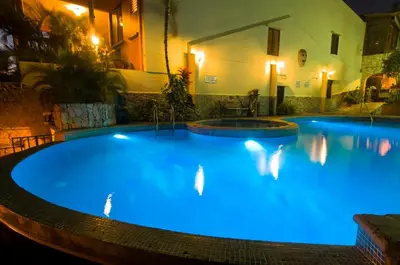 a large blue swimming pool at night with lights at Adventure Inn in San José