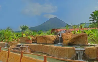 a fountain in a garden with a mountain in the background at Volcano Lodge, Hotel & Thermal Experience in Fortuna