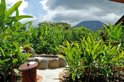 a garden with a stone fountain with mountains in the background at Volcano Lodge, Hotel & Thermal Experience in Fortuna