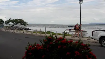 two people standing next to a boat on the water at Atardecer porteño in Puntarenas