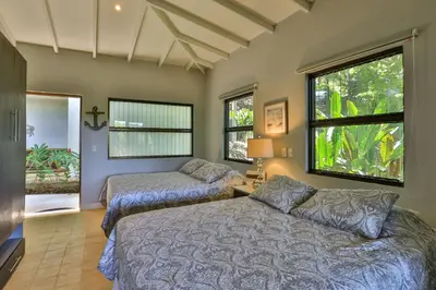 two beds in a room with two windows at Casa de Paz- Portasol Vacation Rentals in Matapalo