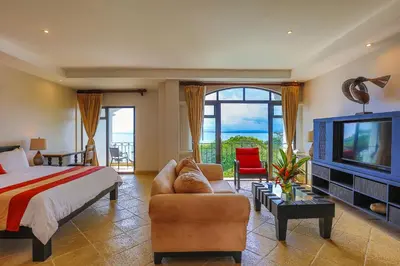 a bedroom with a bed and a couch and a tv at Shana by the Beach Manuel Antonio in Manuel Antonio
