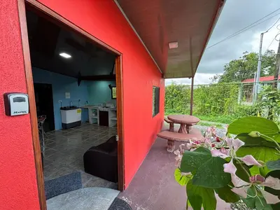 an open door to a red house with a table and a bench at Pura Vida Aparment - Downtown La Fortuna in Fortuna