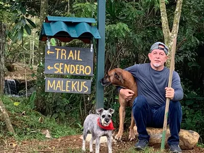 a man sitting next to two dogs in front of a sign at Malekus Mountain Lodge in Aguas Claras