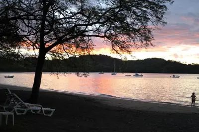 a person standing on a beach near the water with boats at CC Beach Front Papagayo All Inclusive in Papagayo, Guanacaste