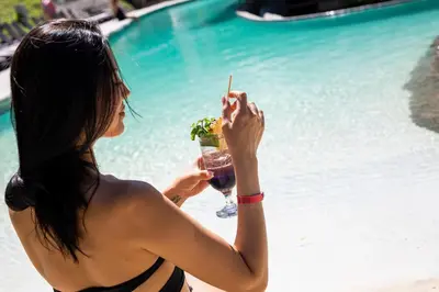 a woman holding a drink next to a swimming pool at Villas Sol Beach Resort in Playa Hermosa