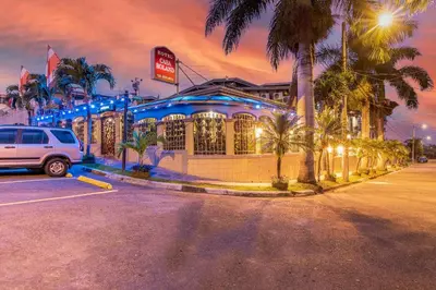 a car parked in front of a building with palm trees at Hotel Casa Roland San Jose in San José
