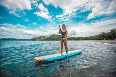a woman standing on a paddle board in the water at Hotel Bosque del Mar Playa Hermosa in Playa Hermosa