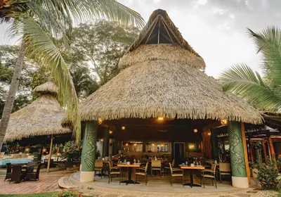 a restaurant with tables and chairs and a thatched roof at Bahia del Sol Beach front Boutique Hotel in Potrero