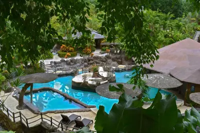 a pool in a backyard with a waterfall and chairs and trees at Hotel Los Lagos Spa & Resort in Fortuna