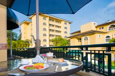 a table with plates of food on a balcony with an umbrella at Apartotel & Suites Villas del Rio in San José