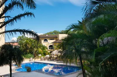 a swimming pool with palm trees in front of a building at Apartotel & Suites Villas del Rio in San José