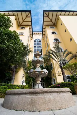 a fountain in front of a building with palm trees at Apartotel & Suites Villas del Rio in San José