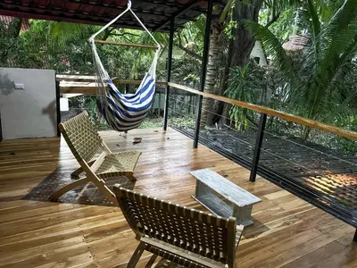 a hammock on a deck with two chairs and a bench at Calala Lodge in Cabuya