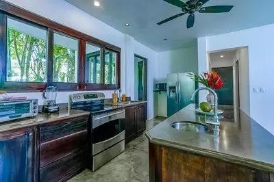 a kitchen with wooden cabinets and a ceiling fan at Makara Rio Suite / Ground Floor in Uvita