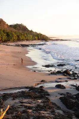 a person walking on a beach next to the ocean at Hotel Nya in Montezuma