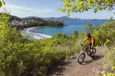 a man riding a bike down a dirt road next to a beach at Santarena Hotel at Las Catalinas in Playa Flamingo