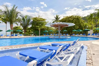 a pool with blue and white lounge chairs and an umbrella at Hotel Punta Leona in Jacó