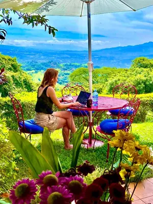 a woman sitting at a table with a laptop at Magic Mountain Views Villa in Atenas