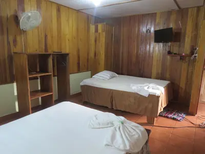 a room with two beds and a tv and wooden walls at Poponjoche Lodge Caño Negro in Caño Negro