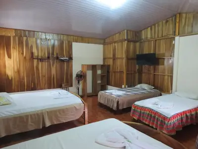 a room with two beds and a tv and wooden walls at Poponjoche Lodge Caño Negro in Caño Negro