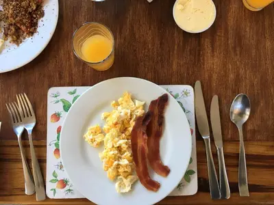 a plate of scrambled eggs and bacon with a glass of orange juice at Poas Volcano Lodge in Vara Blanca