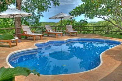 a swimming pool with chairs and umbrellas on a patio at Hacienda Barrigona in Sámara