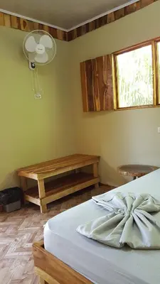 a bedroom with a bed and a table and a window at El Gecko Hotel & Tours in Paquera