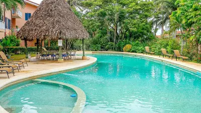 a swimming pool with chairs and a straw umbrella at BL10 Bahia Langosta On the Beach 1bed+1bath in Tamarindo