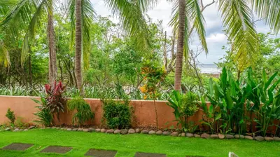 a garden with palm trees and a retaining wall at BL10 Bahia Langosta On the Beach 1bed+1bath in Tamarindo