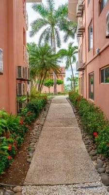 a walkway between two buildings with palm trees and flowers at BL10 Bahia Langosta On the Beach 1bed+1bath in Tamarindo