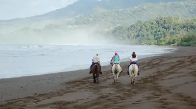 three people are riding horses on the beach at Hotel Villas Rio Mar in Dominical