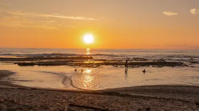 a sunset on the beach with people in the water at Paradise Beach Lodge in Mal País