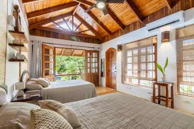 two beds in a room with wooden ceilings and windows at Blue Surf Sanctuary in Santa Teresa Beach