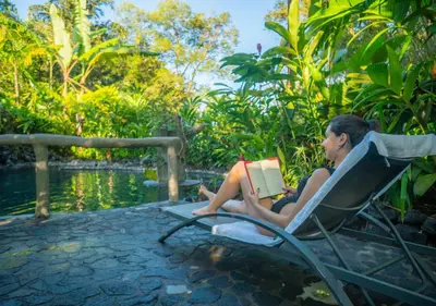a woman sitting in a chair reading a book at Montaña de fuego Mountain Resort & Spa in Fortuna