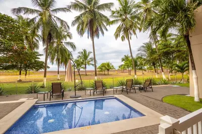 a swimming pool with chairs and palm trees at Oceanfront The Palms Jaco in Jacó