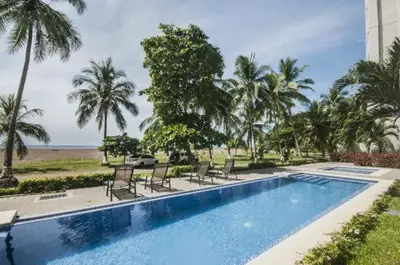a swimming pool with chairs and palm trees at Oceanfront The Palms Jaco in Jacó