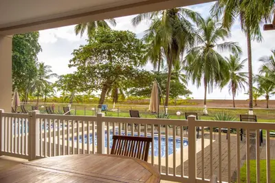 a balcony with a table and a pool and palm trees at Oceanfront The Palms Jaco in Jacó