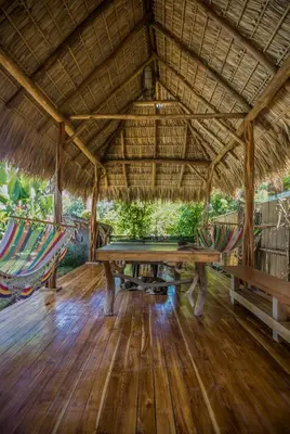 a dining area with a table and hammocks in a straw roof at El Chante Surf House in Santa Teresa Beach