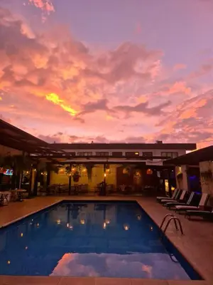 a large swimming pool with a sunset in the background at KC Hotel San Jose in San José