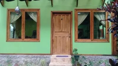 a green house with two windows and a wooden door at casa chilamates in Tortuguero