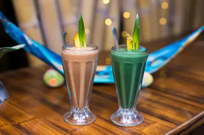 two drinks sitting on top of a wooden table at El Sano Banano Beachside Hotel in Montezuma
