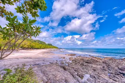a beach with rocks and the ocean on a cloudy day at El Sano Banano Beachside Hotel in Montezuma