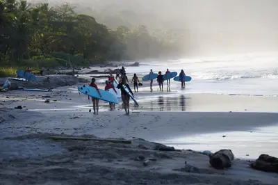 a group of people walking on the beach with surfboards at Hotel Santa Teresa by the Beach in Santa Teresa Beach
