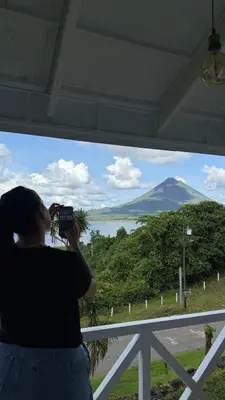 a woman taking a picture of a mountain from a window at Hotel Arenal Vista Lodge in Fortuna